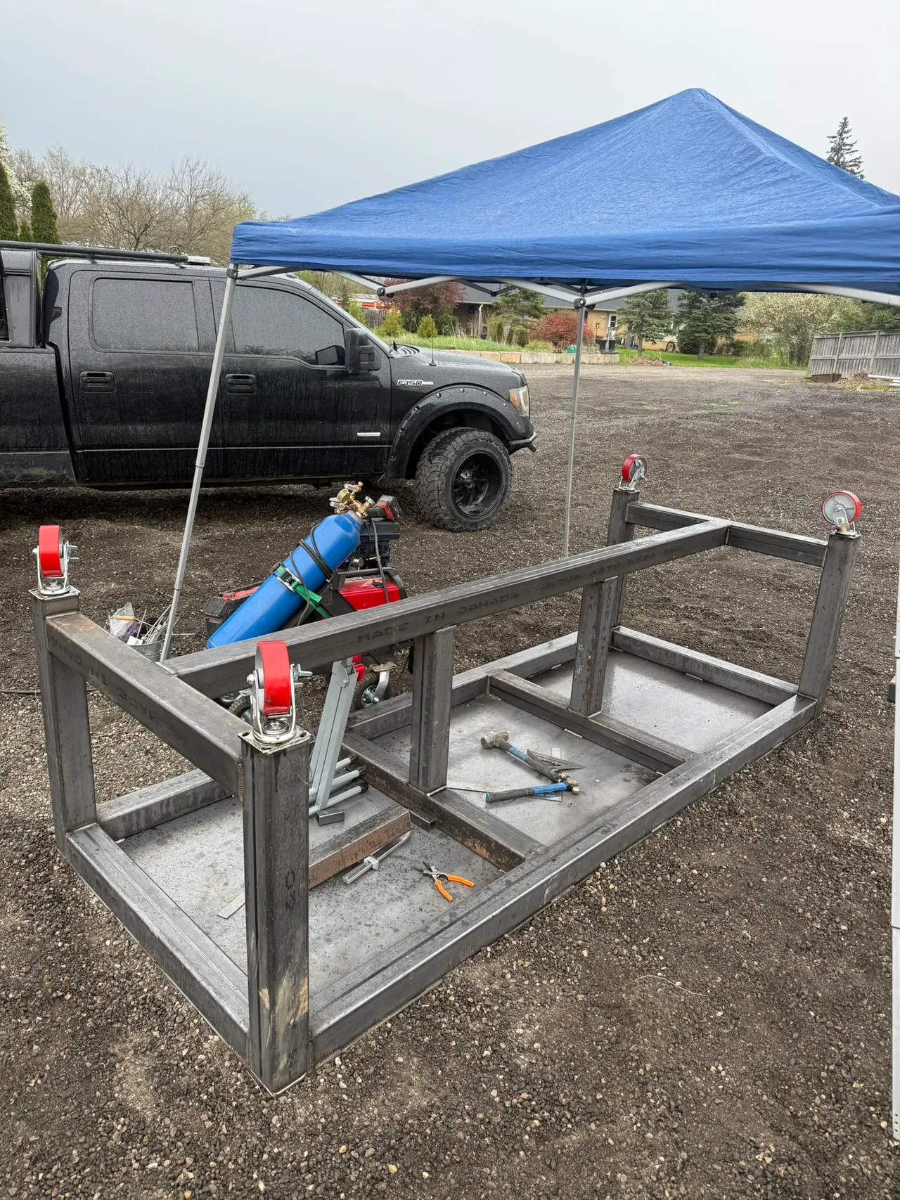 Steel welding table being fabricated beside the mobile welding truck under a blue canopy