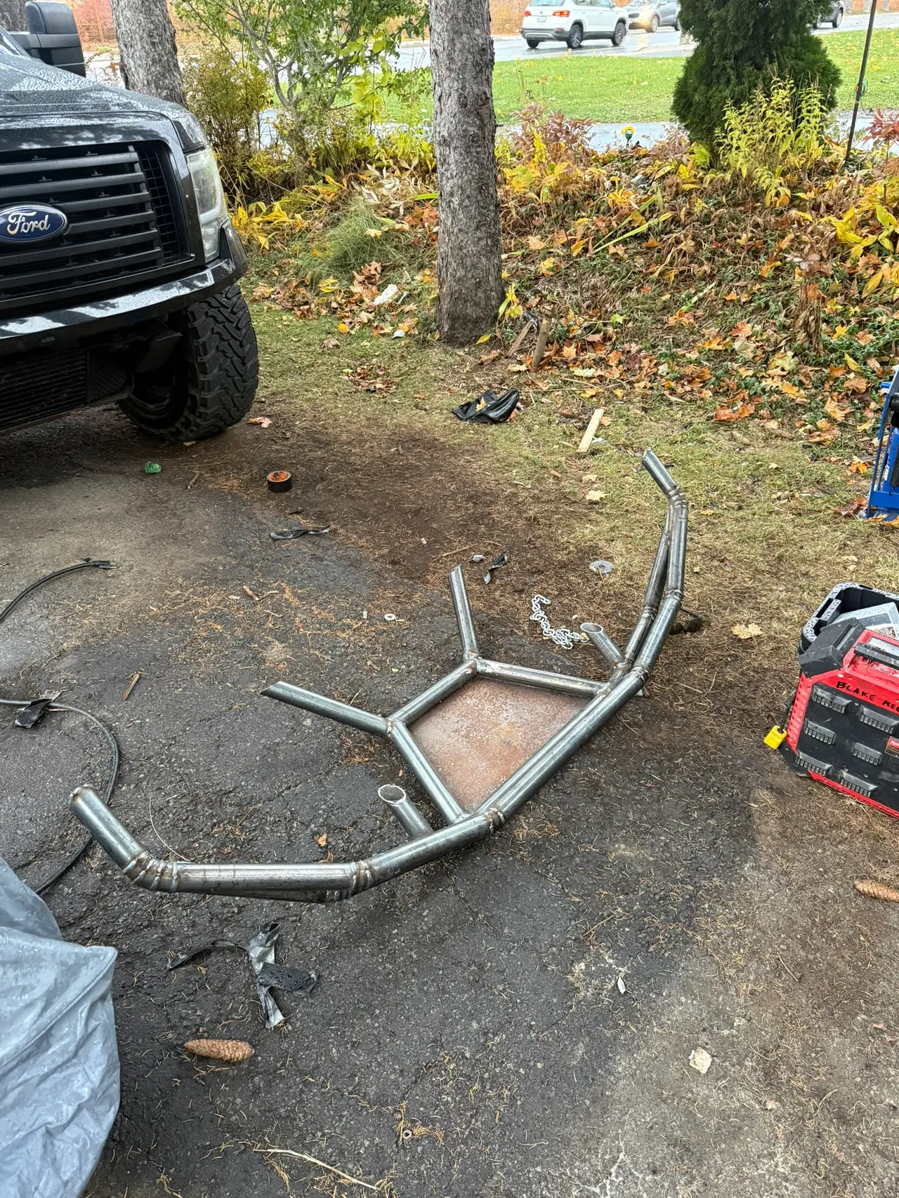 Bent steel tube bumper with welded supports laid out in front of a truck